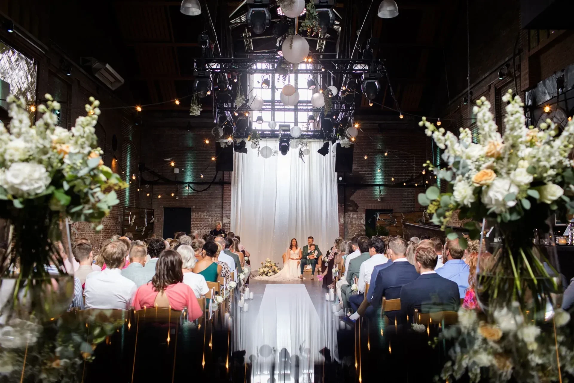Een ceremonie van een bruid en bruidegom met heel veel mensen en bloemen om hun heen.
