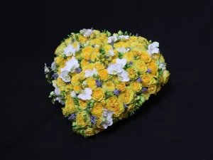 Rouwstuk Yellow Heart. Een bloemstuk in de vorm van een hart, met gele, witte en paarse bloemen. Gemaakt door Bloeibloemen.nl