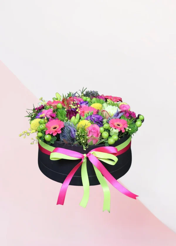 Flower box Color Big, een box met verschillende soorten bloemen in de kleuren geel, roze, paars, rood en groen, gestoken in een blok oase. Deze bloemen zitten in een zwarte box met roze en groen lint eromheen.