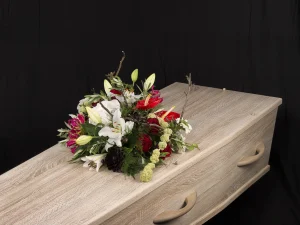 Rouwstuk Red and white, een rouw bloemstuk op een kist met bloemen in de kleuren wit, groen en rood, gemaakt door Bloeibloemen.nl