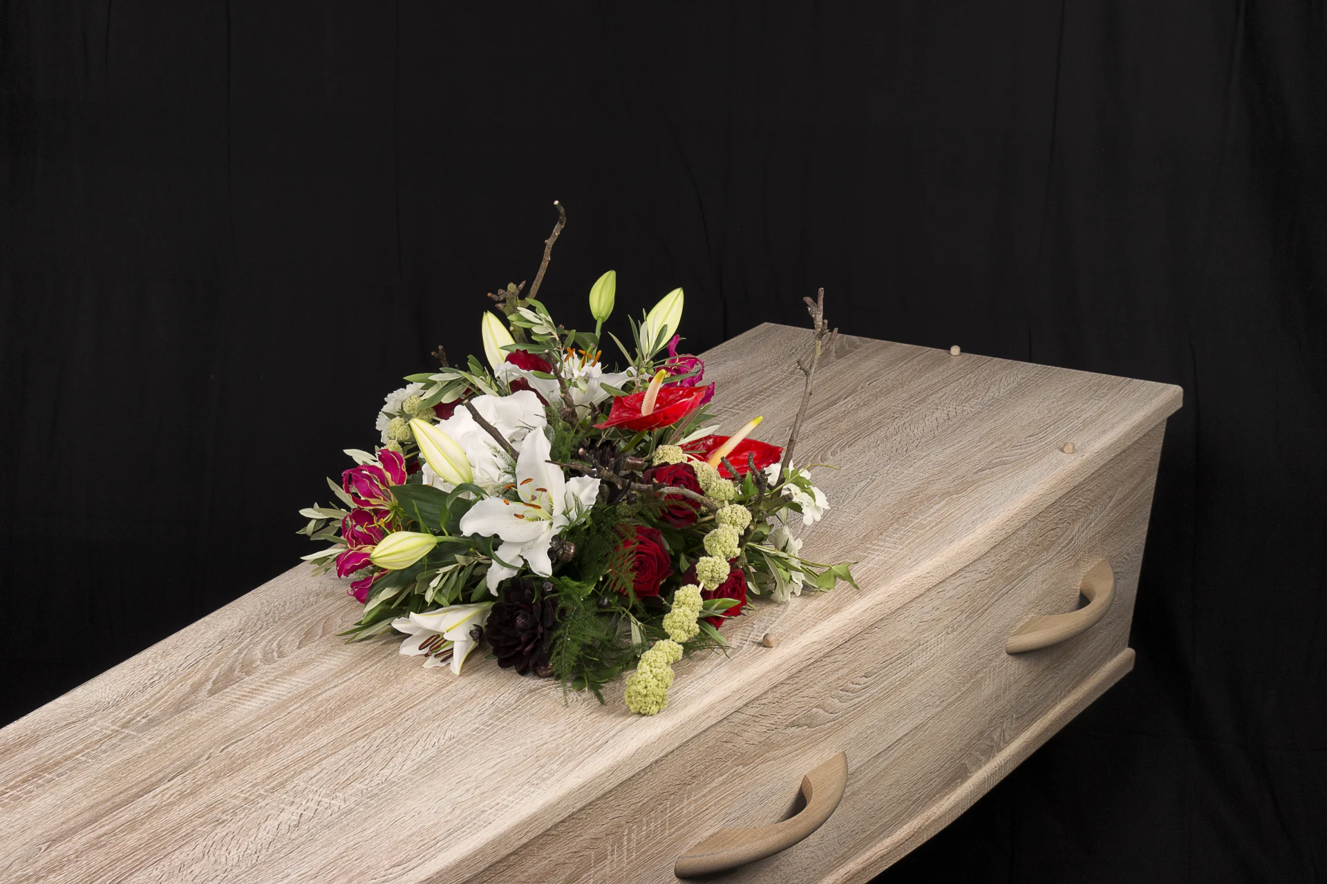 Rouwstuk Red and white, een rouw bloemstuk op een kist met bloemen in de kleuren wit, groen en rood, gemaakt door Bloeibloemen.nl